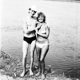 Couple stands by a lake, wearing swimwear.