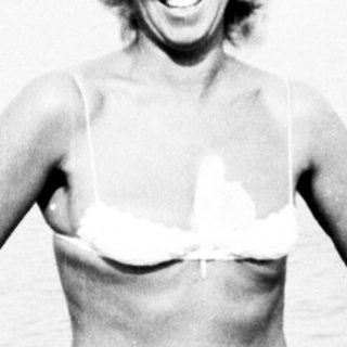 Woman in bikini stands near a lake, smiling.