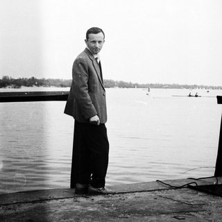 Man stands near water, wearing a suit and tie.