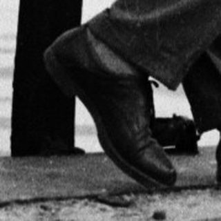 Man in suit standing on a pier overlooking water.