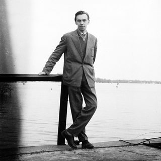 Man in suit standing on a pier overlooking water.