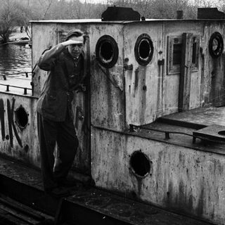 Man stands in a weathered, industrial-looking structure near water.