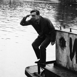 Man stands on a structure over water, with trees in background.