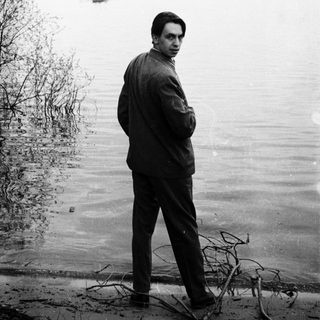 Man stands near water, looking over a body of water.