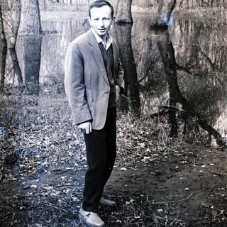 Man in suit stands near trees, captured in a vintage photograph.