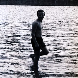 Man wading in water, boat visible in the background.