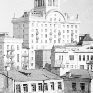 Here's a brief summary of the image: Historic cityscape with buildings and rooftops in a vintage photo.