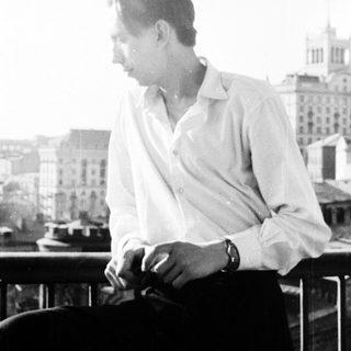 Man in shirt sits on balcony overlooking a city.