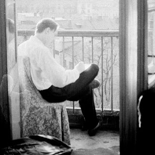 Man seated on balcony, appears to be reading or writing.