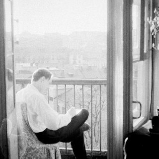 Man seated on balcony, appears to be reading or writing.