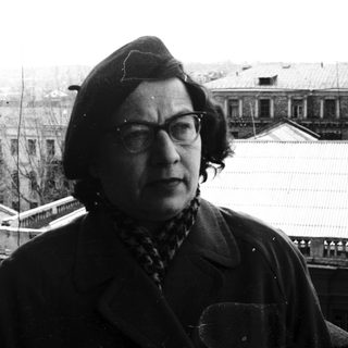 Man in a hat stands on a rooftop overlooking buildings.