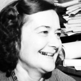 Smiling woman seated near a desk and bookshelves.