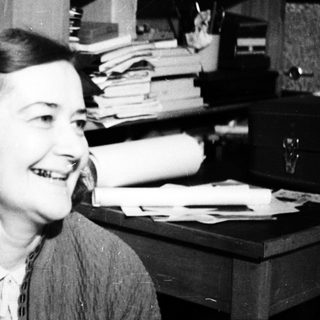 Smiling woman seated near a desk and bookshelves.