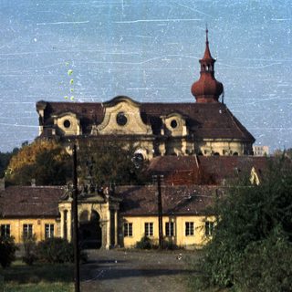 Old building with a tower, seen through trees.