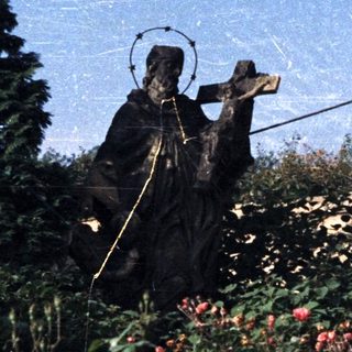 Statue of a religious figure amid overgrown foliage and ruins.
