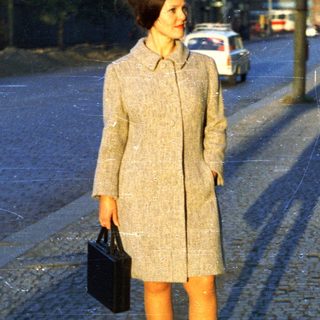 Woman in coat stands on a cobblestone street.