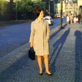 Woman in coat stands on a cobblestone street.