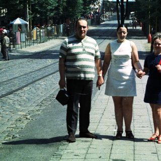 Three people walk down a cobblestone street in a city.