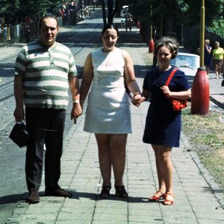 Three people walk down a cobblestone street in a city.