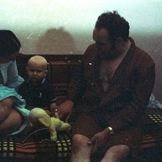 Woman, baby, and man seated on a colorful rug.