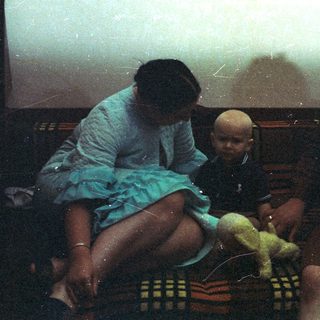 Woman, baby, and man seated on a colorful rug.