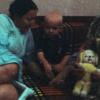 A child sits with two adults on a rug.