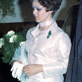 Bride, groom, and attendants stand indoors, likely at a wedding.