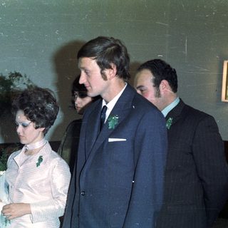 Bride, groom, and attendants stand indoors, likely at a wedding.