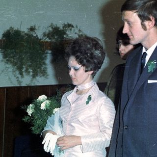 Bride, groom, and attendants stand indoors, likely at a wedding.
