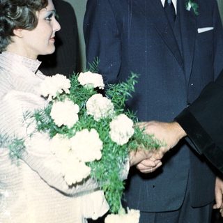 Man in suit shakes hands with woman holding flowers.