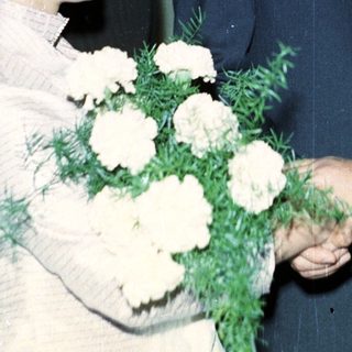 Man in suit shakes hands with woman holding flowers.