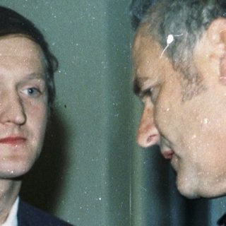 Man in suit shakes hands with woman holding flowers.