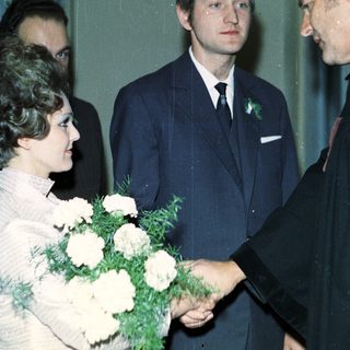 Man in suit shakes hands with woman holding flowers.