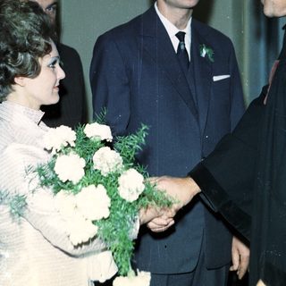 Man in suit shakes hands with woman holding flowers.