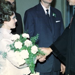 Man in suit shakes hands with woman holding flowers.