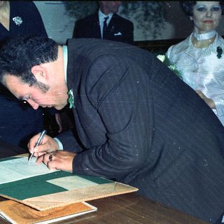Man signing document, possibly at a formal event.
