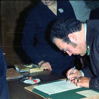 Man signing document, possibly at a formal event.