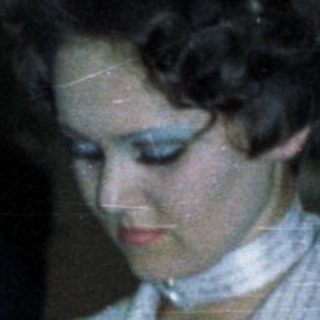 Woman signs document with onlookers during an event.