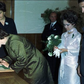 Woman signs document with onlookers during an event.