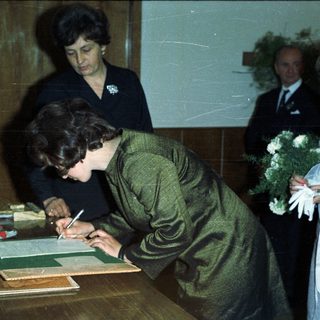 Woman signs document with onlookers during an event.
