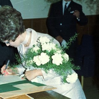 Woman signing document, likely a marriage certificate, with onlookers.