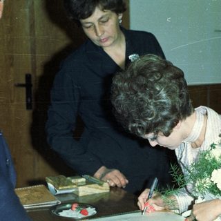Woman signing document, likely a marriage certificate, with onlookers.
