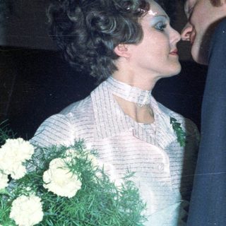 Couple embraces during a wedding, surrounded by guests.