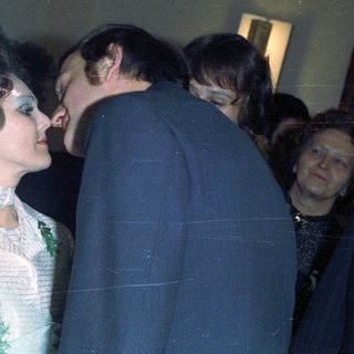 Couple embraces during a wedding, surrounded by guests.