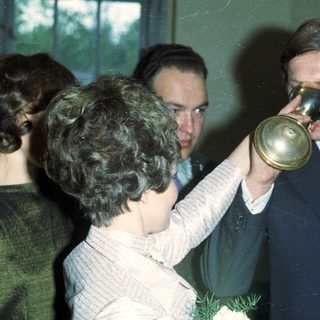 Man drinks from a horn, surrounded by people.