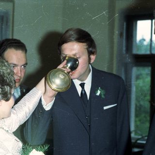 Man drinks from a horn, surrounded by people.