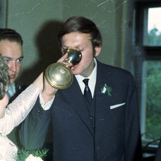 Man drinks from a horn, surrounded by people.