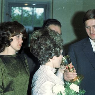 Woman holding trophy with man and others nearby.