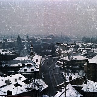 Snow-covered rooftops and cityscape under a cloudy sky.