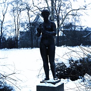 Nude statue stands on a pedestal in a snowy landscape.